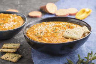 Sweet potato or batata cream soup with sesame seeds and snacks in blue ceramic bowls on a black