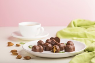 Chocolate caramel candies with almonds and a cup of coffee on a white and pink background and green