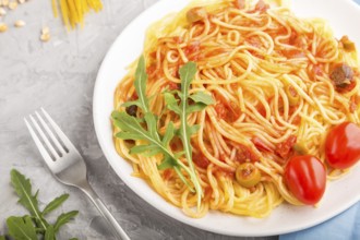 Corn noodles with tomato sauce and arugula on a gray concrete background and blue textile. Side