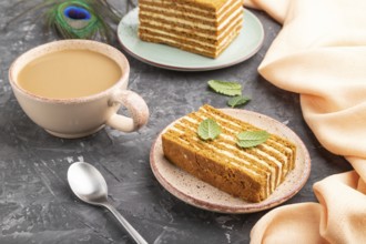 Homemade honey cake with milk cream and mint with cup of coffee on a black concrete background and