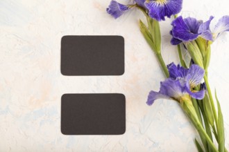 Black business card with blue iris flowers on white concrete background. top view, flat lay, copy