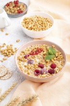 Wheat flakes porridge with milk, raspberry and currant in ceramic bowl on gray concrete background