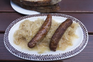 Two Nuremberg sausages with cabbage and bread on an oval plate in a garden restaurant, Bavaria,