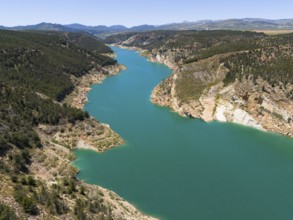 A river crosses a wooded and mountainous landscape, the water appears blue and calm, aerial view,