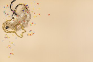 Golden mask and chain on a beige background with scattered confetti, carnival