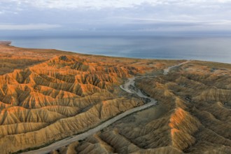 River bed runs through a landscape of eroded hills, badlands at sunset, Lake Issyk Kul in the