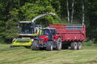 Tractor with trailer running beside Claas Jaguar 870 forage harvester, self-propelled silage