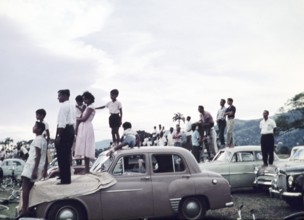 People standing on cars to watch a school sporting event - annual football match between Queen