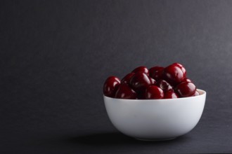 Fresh red sweet cherry in white bowl on black background. side view, copy space