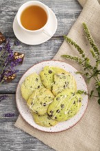 Green cookies with chocolate and mint on ceramic plate with cup of green tea and linen textile on