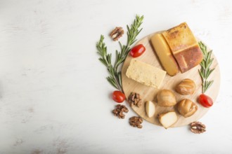 Smoked cheese and various types of cheese with rosemary and tomatoes on wooden board on a white