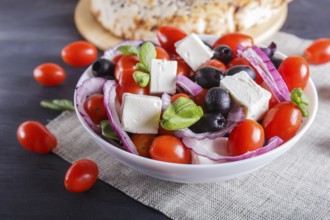 Greek salad with fresh cherry tomatoes, feta cheese, black olives, basil and onion on black wooden