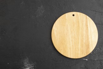 Empty round wooden cutting board on black concrete background. Top view, copy space, flat lay