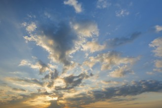 Sun breaks through cloud cover and illuminates fleecy clouds in the evening blue sky