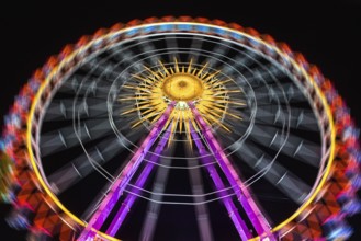 Illuminated Ferris wheel at night in bright neon colours against a dark sky, Cannstatter Volksfest,