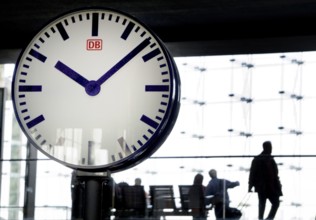 Large station clock, Deutsche Bahn passengers sitting on a bench at Berlin Central Station,