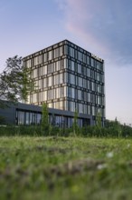 Modern office building with glass façade in a green environment with evening lighting, Nagold