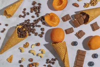 Ice cream cones with coffee beans, apricots, nuts and chocolate on a marble background