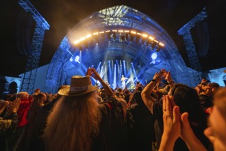 Concertgoers applaud at a night-time concert with blue lights on stage, Klostersommer, Calw Hirsau,