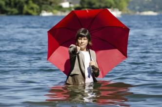 Elegant Business Woman with Suit Standing in the Water and Holding a Red Umbrella