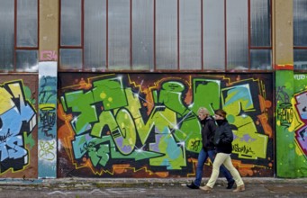 Two people walking along a wall covered with colourful graffiti, urban ambience, Landau,