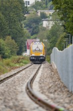 A train on rails runs through a landscape with trees, the atmosphere is autumnal and quiet, track