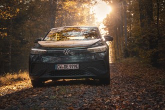 Car in the golden light of the evening sun on an autumnal forest path with leaves, electric car VW