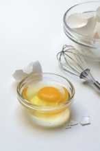 Egg whites and egg yolks in glass bowl and egg shells, whisk