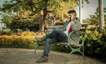 Man sitting on a bench calling on the phone, young man sitting on a bench with cell phone, close up