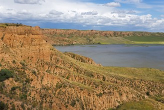 Ein felsiger Canyon, der sich entlang eines Sees erstreckt, unter einem überwiegend blauen Himmel