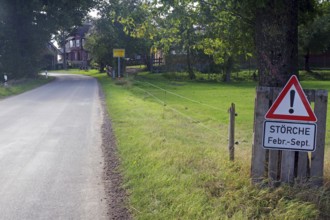 Country road with a warning sign for storks in a green village, Wendland, Elbe, Germany, Europe