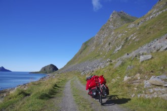 Cycling on a gravel road along the sea with a view of mountains and a bright blue sky, cycling