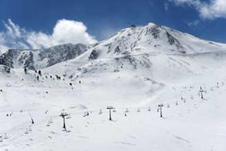 Schneebedeckte Berge unter blauem Himmel, mit Skiliften und einigen Skifahrern auf den Pisten,