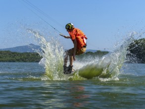 Young casual man with flapping shirt on wakeboard jumping into the lake, water ski and wakepark,