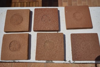 Six square clay bricks with different geometric and floral patterns laid on a white table top,