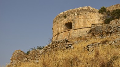 An old, round stone tower stands on a hill with overgrown vegetation, Venetian sea fortress, Leper