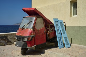 Weathered red tricycle next to blue shutters on the coast, Mandraki, Nisyros, Dodecanese, Greek