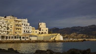 Coastal town in the morning light with buildings and mountains in the background, Pigadia, town and