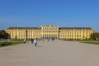 Schönbrunn Palace with yellow facade and blue sky in the background, some tourists in the