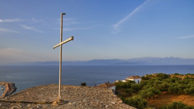 Cross on a hill overlooking the sea and the coastal landscape in the evening light, Koroni,