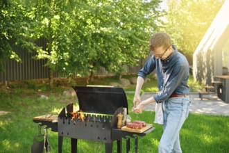 Middle-aged man sprinkles raw steak with sea salt using hand mill while cooking at backyard