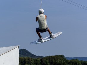 Young man jumping with wakeboard over jump and obstacle, water sports, water skiing in wakepark,