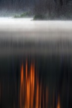 Reflection of orange-coloured light on foggy water in a gloomy landscape, foggy atmosphere over the