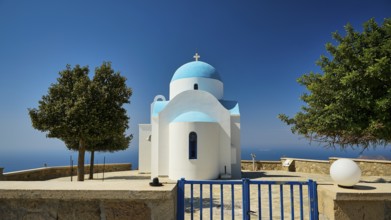 White-blue church behind a lattice gate with surrounding trees under a blue sky, Profitis Ilias