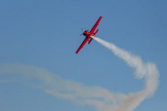 Red stunt aerobatic plane performing stunts in blue sky. Concept of speed, difficulty, precision,