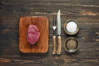 A fresh prime cut of beef steak on a chopping board, next to bowls of salt and pepper, with a