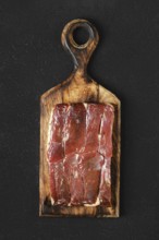 Juicy block of cured duck meat on a handcrafted wooden cutting board against a dark background