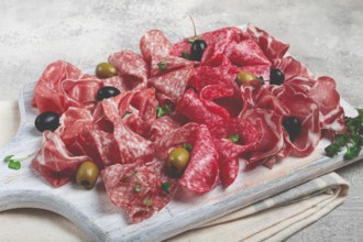 Assorted, meat appetizer, prosciutto, salami and ham, with olives, on a wooden white board, light