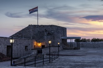 Old fortress with Croatian flag and illuminated lanterns in the evening light, Hvar, Croatia,