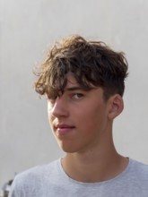 Portrait of a young athletic man with curly brown hair in front of a grey wall, looking into the